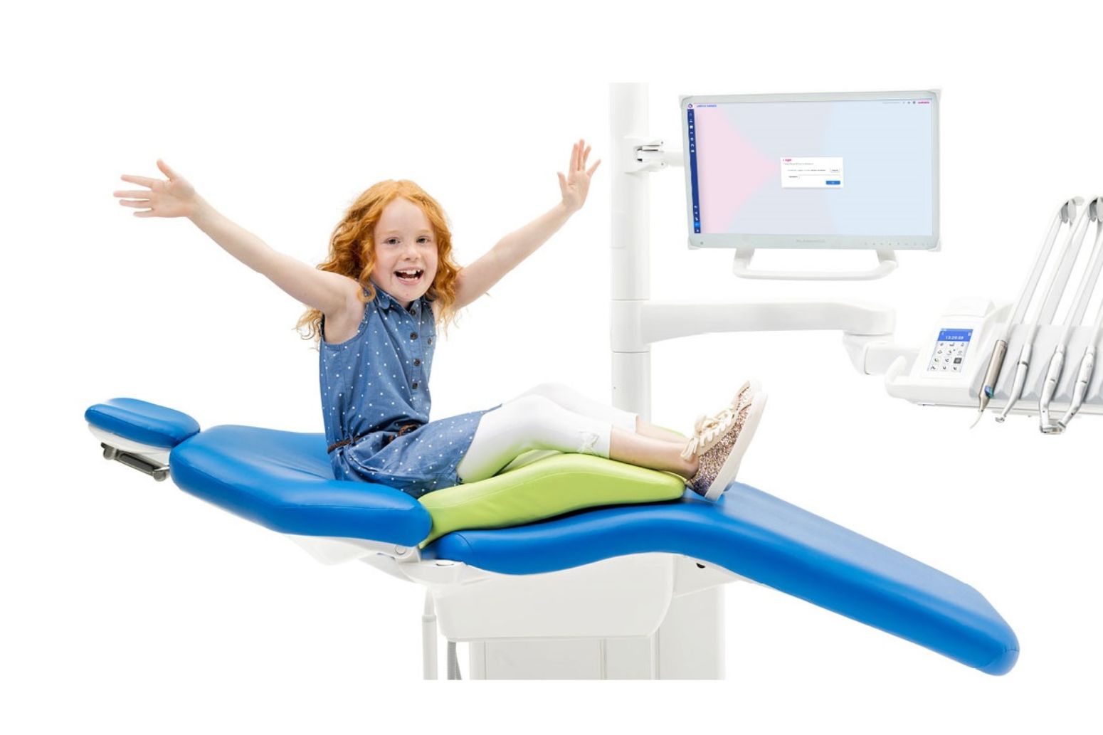 Glad pige sidder med armene udstrakt på en tandlæge unit og hun har en pude under sig, så hun sidder ergonomisk korrekt